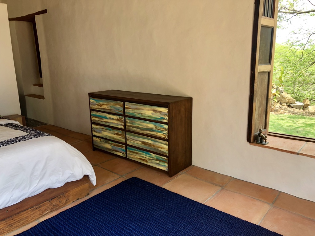 Painted wooden dresser beside the bed with a window onto the garden
