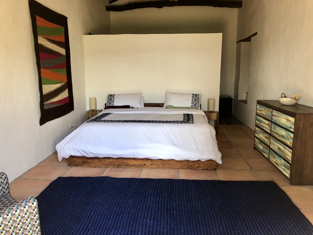 King bed on a reclaimed timber base with a striped Colombian tapestry and painted dresser