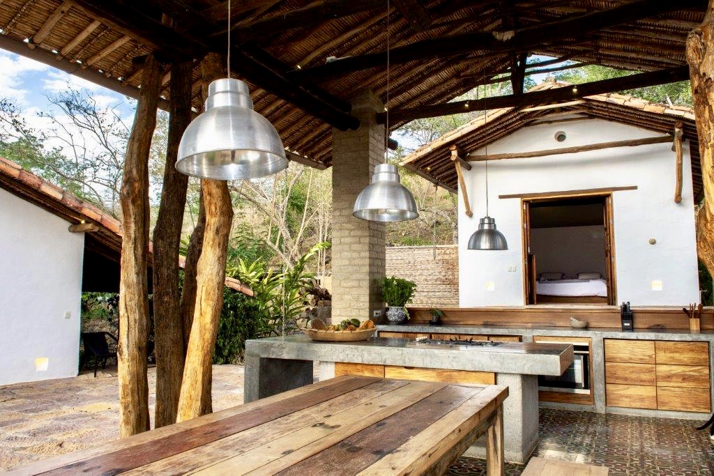 Outdoor kitchen pavilion with concrete island, reclaimed wood table and industrial pendant lamps
