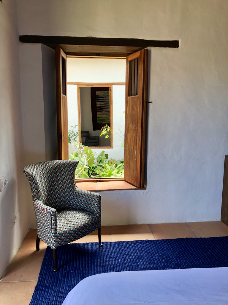 Patterned armchair beside a timber window looking onto the planted courtyard
