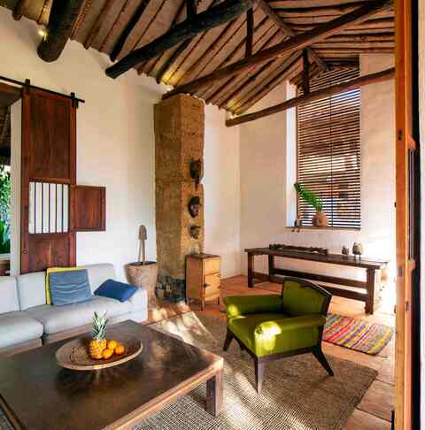 Living room corner with a stone column, green armchair and carved wooden console beneath the beamed roof