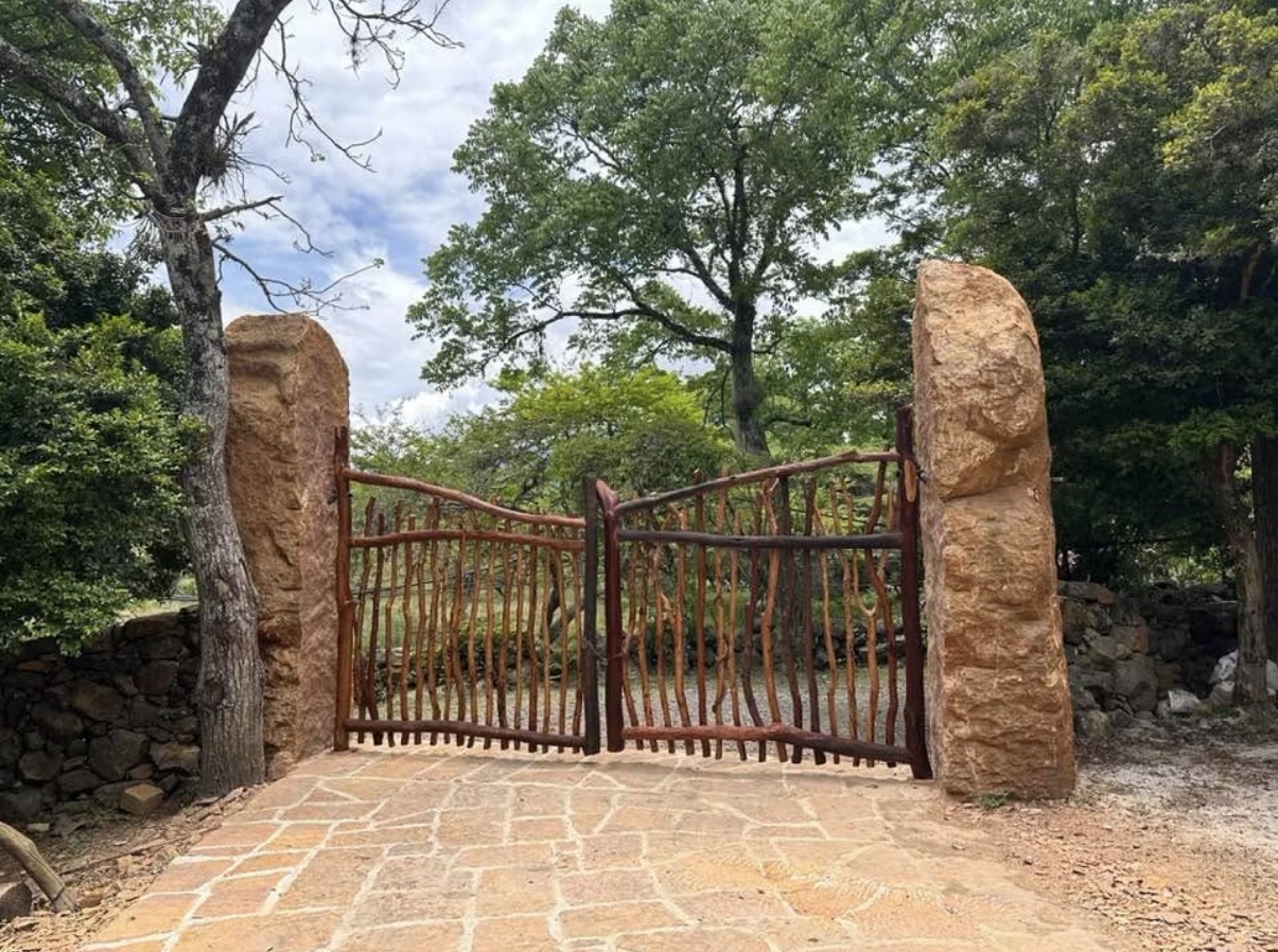 Hand-built branch gate set between two standing sandstone boulders at the finca entrance