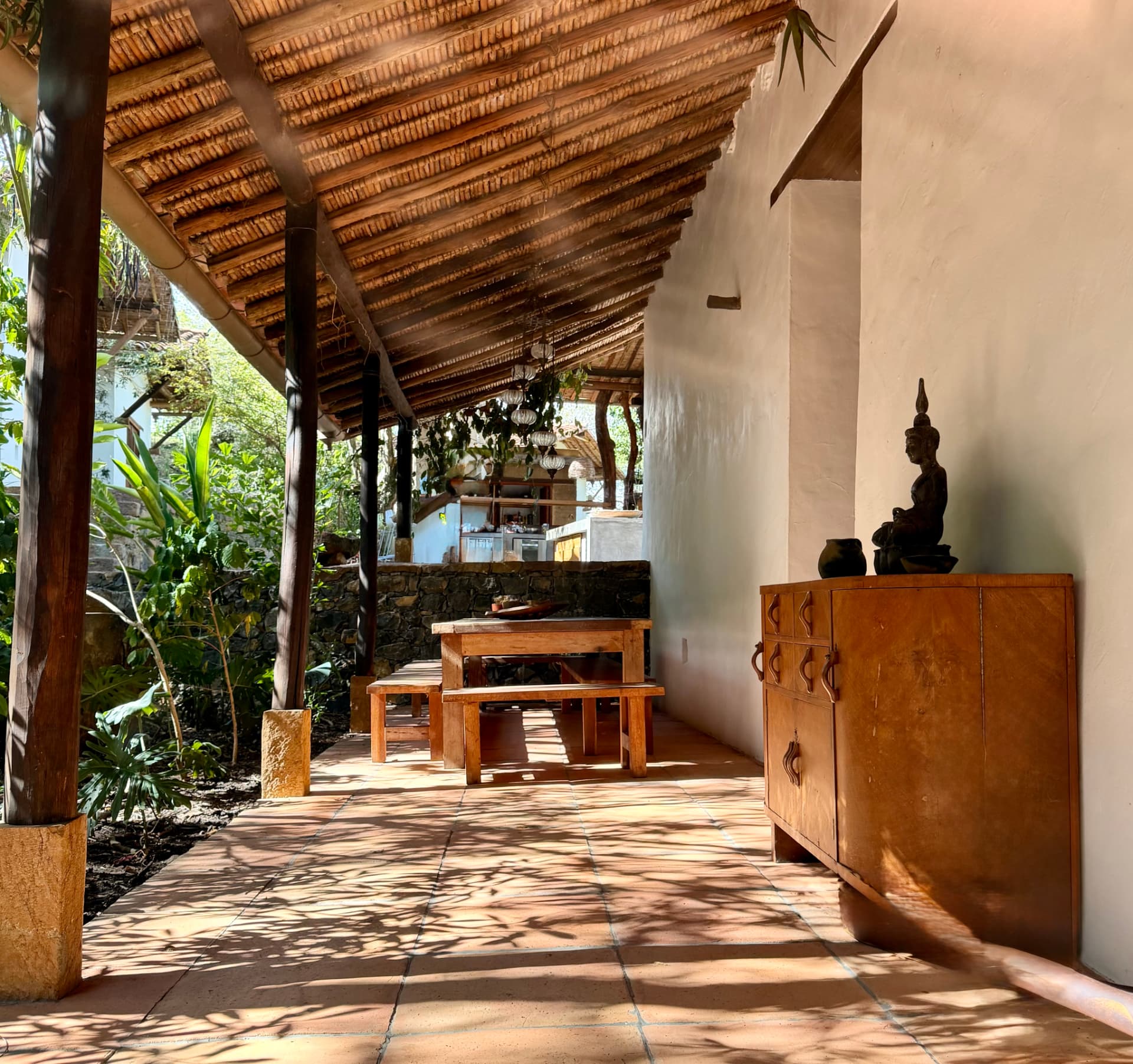 Covered walkway with terracotta tiles, timber ceiling and a carved wooden cabinet leading to the outdoor kitchen