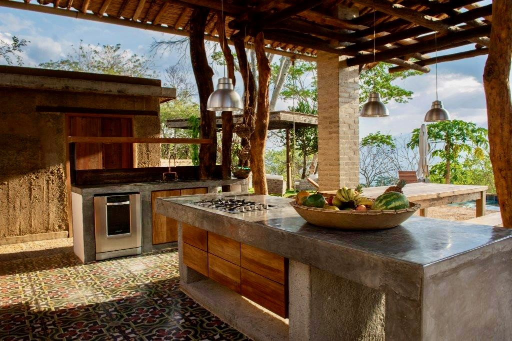 Concrete kitchen island with gas hob and patterned tile floor under the pergola
