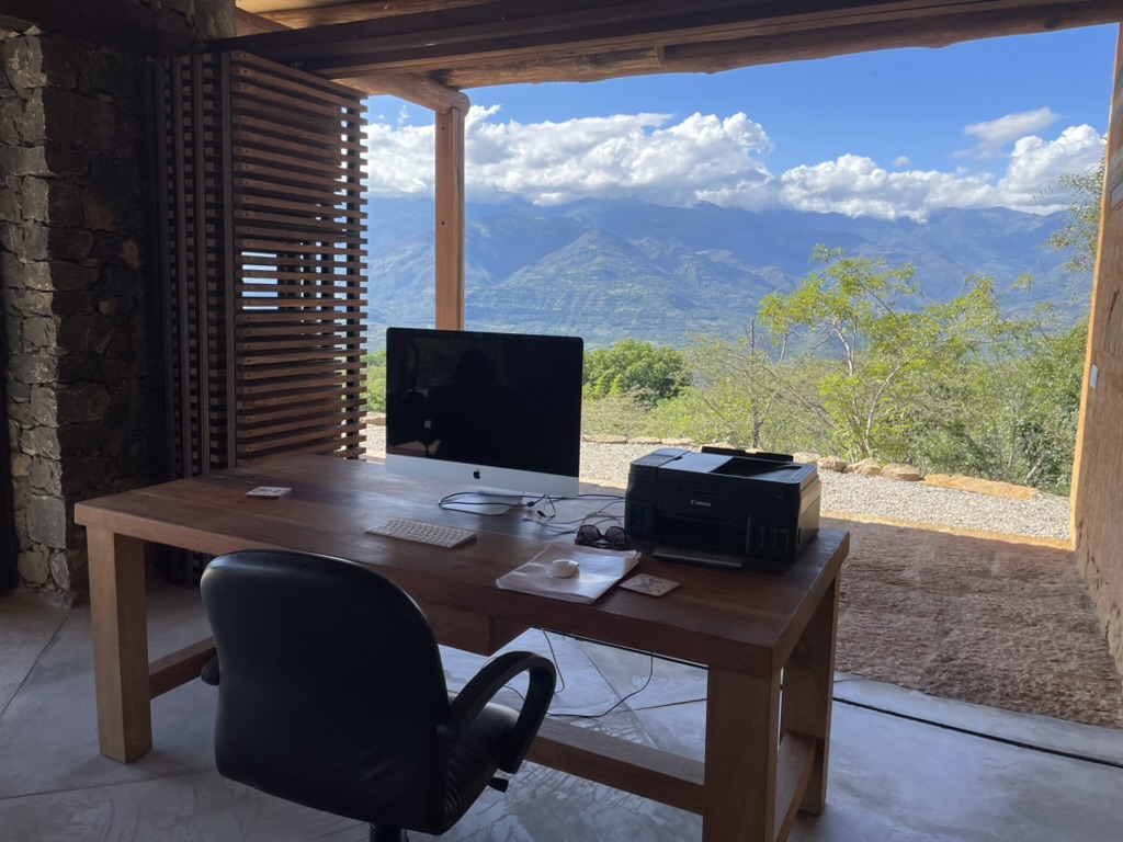 Timber desk and screen beside the open wall, mountains and clouds beyond