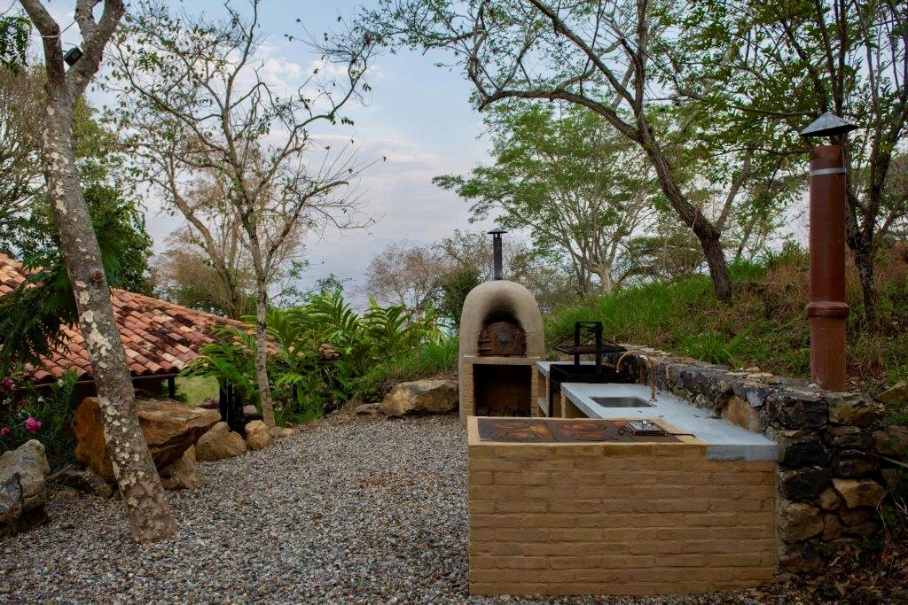 Adobe pizza oven and grill built into a stone wall at the garden's edge