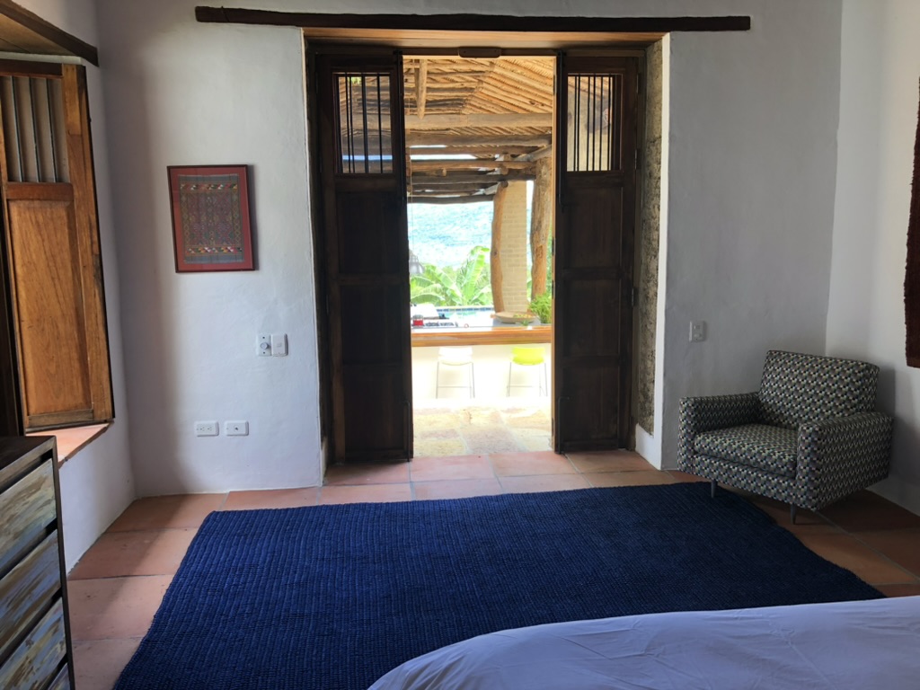 Bedroom with timber doors opening onto the pool terrace and cane-roofed pavilion