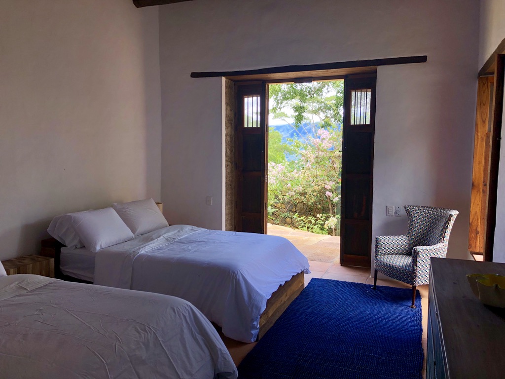 Twin double beds with doors open to flowering trees and mountain views