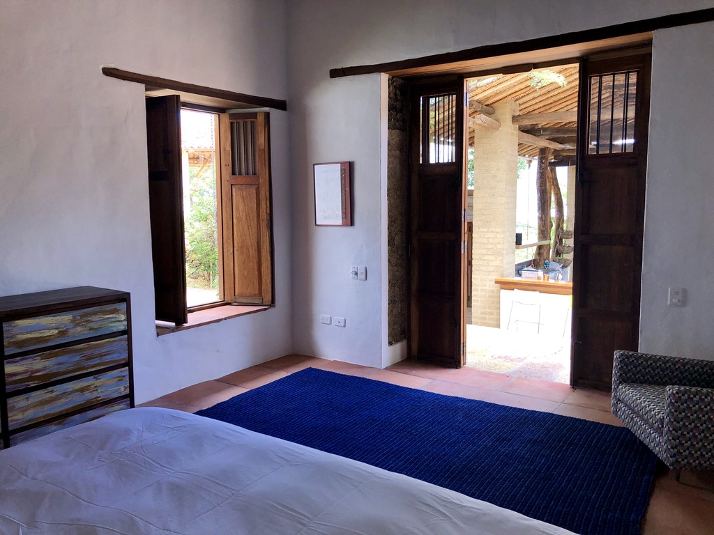 Bedroom with shuttered window and doors open to the outdoor kitchen pavilion